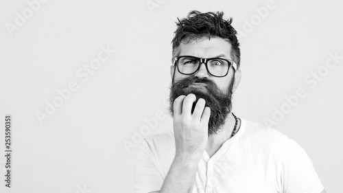 Pensive man touching his beard on white wall. Handsome man in glasses thinks. Emotional bearded guy has a doubt. Human face expressions, emotions, feelings, body language