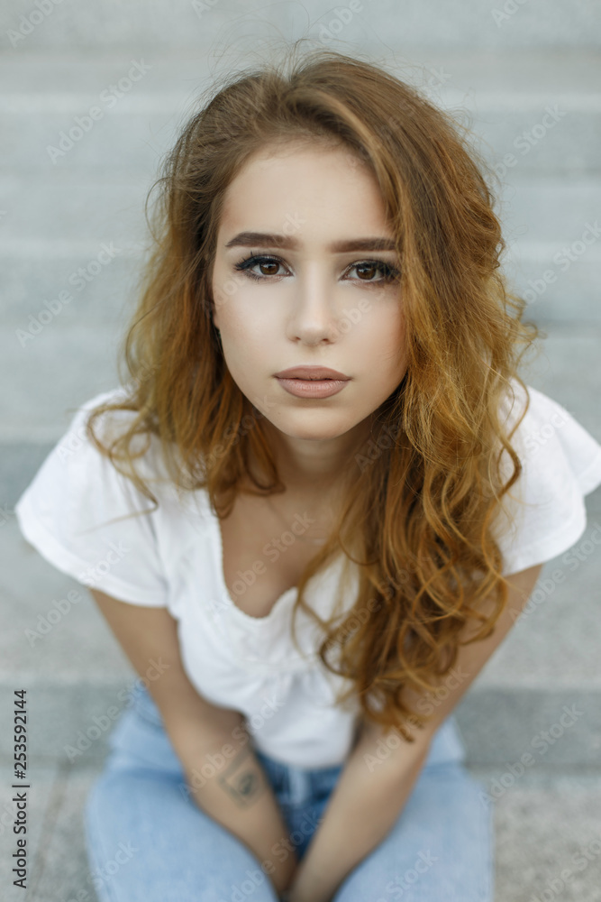 Female face portrait of pretty young attractive woman in fashionable white  t-shirt in jeans with beautiful brown eyes outdoors. Pretty girl model  resting enjoying a warm summer day. Stock Photo