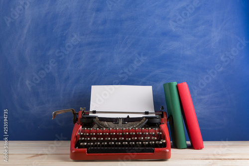 writer's workplace - red typewriter and books on blue blackboard background