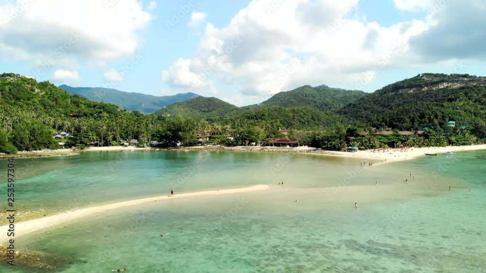 A drone flight over clear waters beach with mountains in the background A drone flight over clear waters beach with mountains in the background