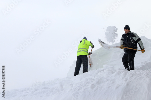Zwei Männer schaufeln hohen, schweren Schnee von einem Hausdach