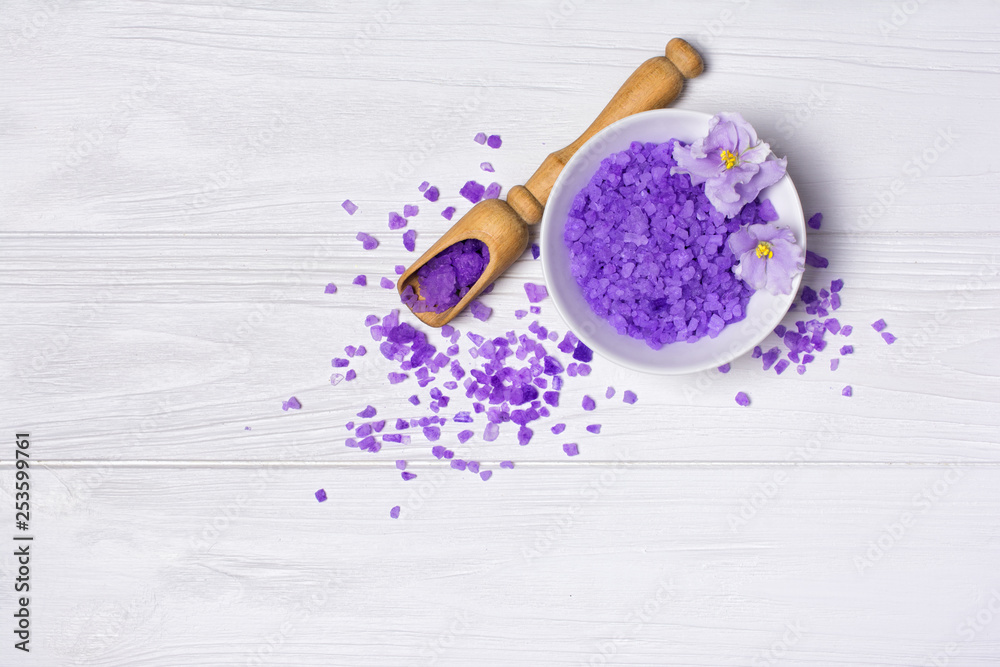 Fototapeta Flavored purple sea salt crystals with violet flower and wooden scoop on white