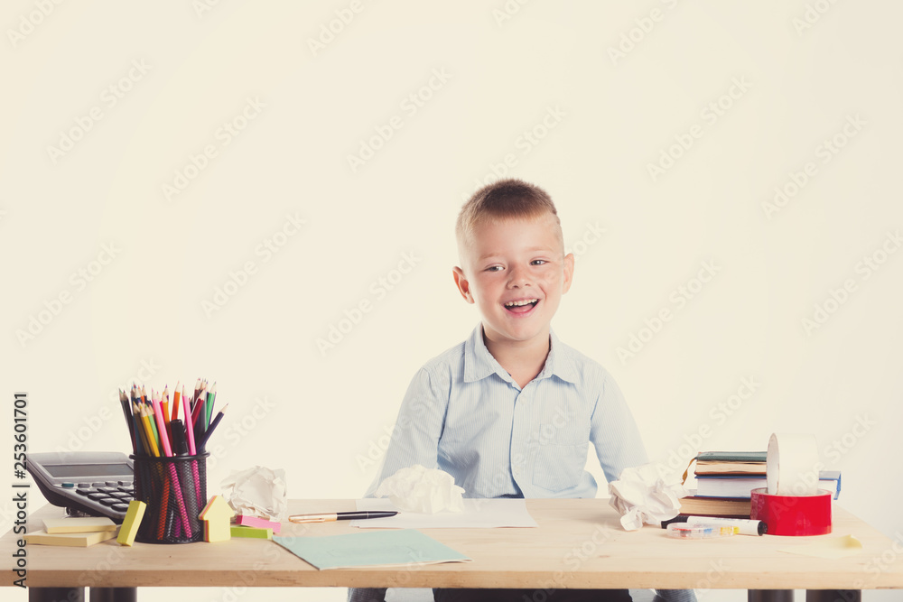 Cute little school boy with huge smile sitting at his desk on white background. Happy intelligent children in shirt Cute little school boy with huge smile sitting at his desk on white background. Happy intelligent children in shirt
