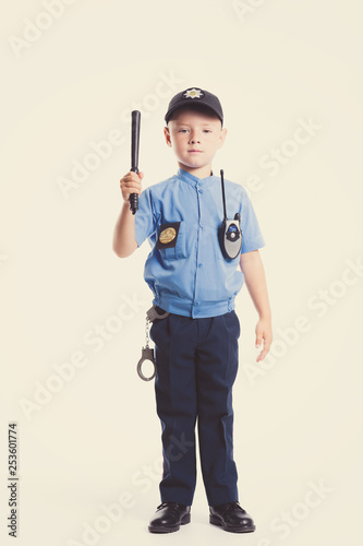Cute little police boy with smile on face and baton on white background. Intelligent cool children in police suit with blue eyes and baton regulates traffic