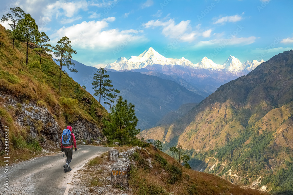 Male tourist backpacker walk through scenic mountain road with view of Himalaya range near Binsar Uttarakhand India.