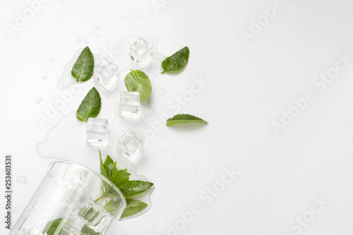 Spilled Glass with refreshing water, mint leaves and ice cubes on a light background