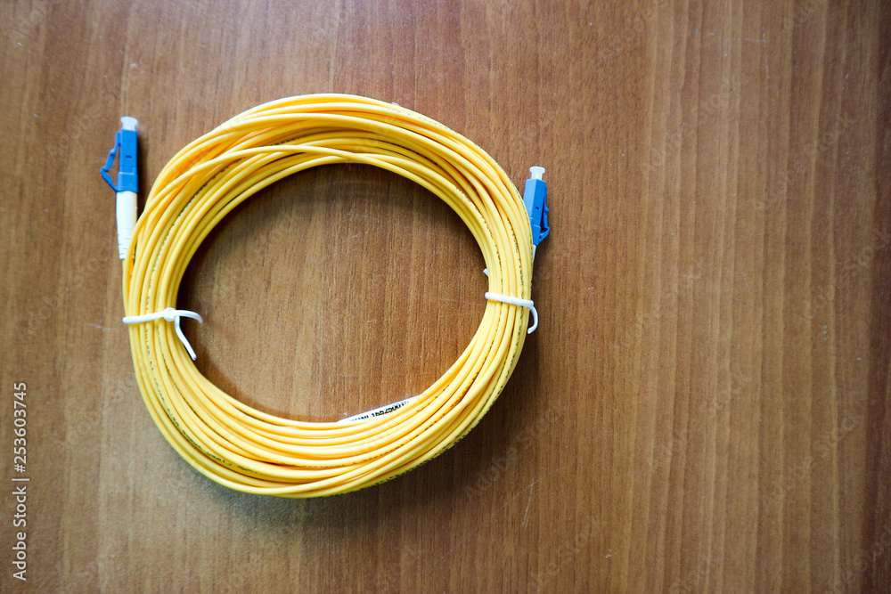 Yellow Fiber optic patch cord lay on wooden table Yellow Fiber optic patch cord lay on wooden table