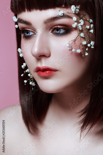 portrait of beautiful young woman with flowers on her face on the wonderful pink studio background