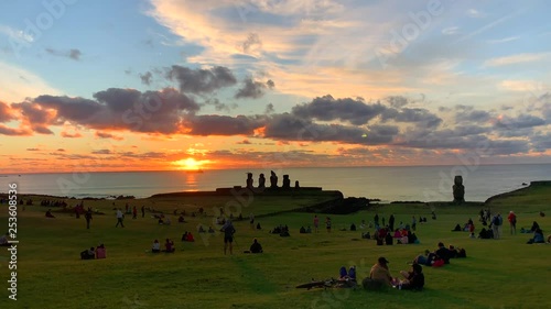 Sunset view of Oceanside Ahu Tahai archaeological complex with restored sculptures and people sitting on grass. Rapa Nui National Park. Isla de Pascua, Easter Island, Chile. photo