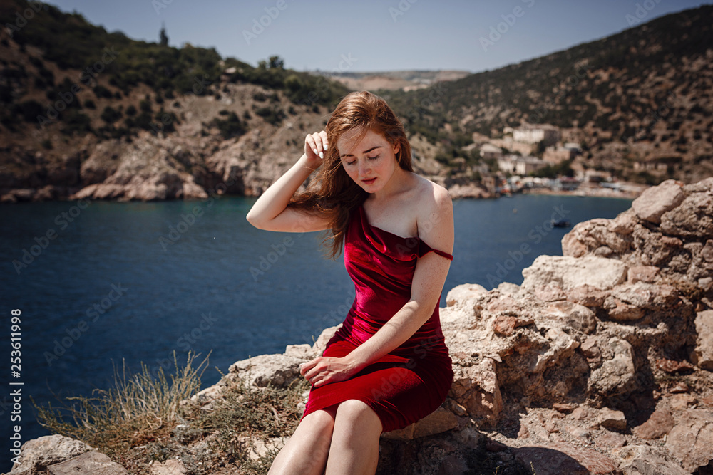 A beautiful red-haired woman is sitting on a rock A beautiful red-haired woman is sitting on a rock