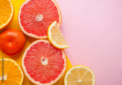 Flat lay of cut ripe juicy grapefruit, lemon and orange on yellow and pink background. Citrus pattern.