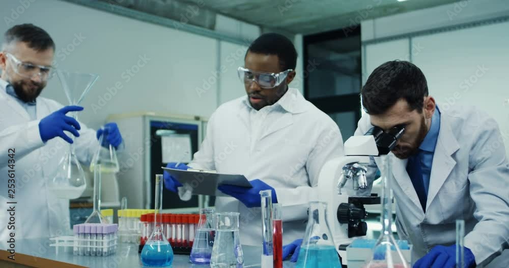 Three multiethnical men scientists working with test tubes and microscope in the modern laboratory. Three multiethnical men scientists working with test tubes and microscope in the modern laboratory.