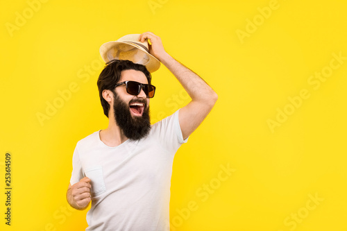 studio portrait of a cheerful bearded guy in a great mood, man in sunglasses, welcome gesture of raising the hat, concept summer vacation