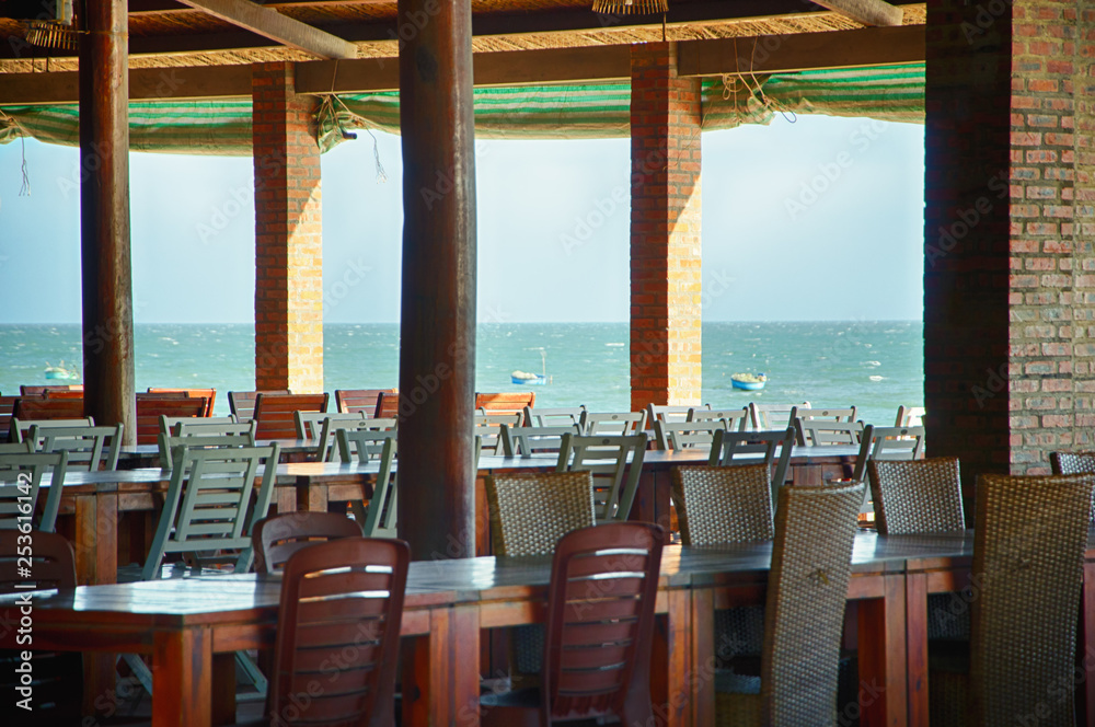 Tables in a cafe under a canopy on the beach. View from the cafe on the Pacific Ocean. Mui Ne village, Province of Binh Thuan, Phan Thiet, Vietnam.