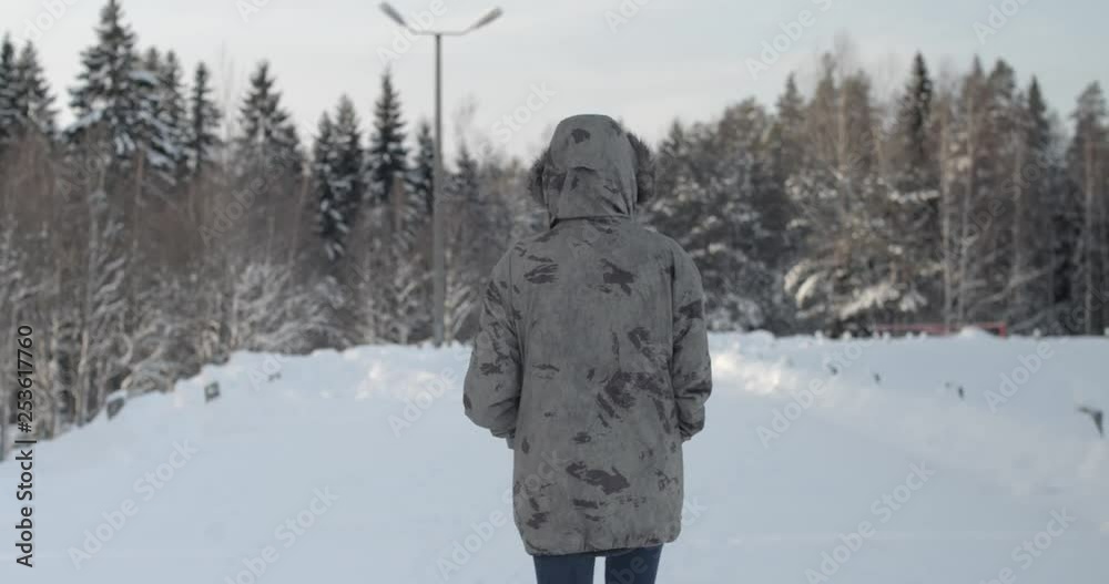 A mid shot that follows behind a tall woman as she wanders along a snow covered road lined by trees smothered in beautifully fresh and glistening white snow. A mid shot that follows behind a tall woman as she wanders along a snow covered road lined by trees smothered in beautifully fresh and glistening white snow.