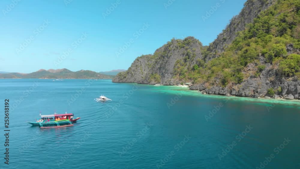 Colorful small boats with outriggers on the calm azure water of the Philippines. Steep rocky shore of one of the many islands of Busuanga jutting out of the water. Tropical island paradise. PAN LEFT. Colorful small boats with outriggers on the calm azure water of the Philippines. Steep rocky shore of one of the many islands of Busuanga jutting out of the water. Tropical island paradise. PAN LEFT.