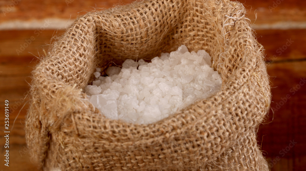 Salt or sea salt in a wooden bowl, burlap sack, bag and scoop on a aged wooden table background.
