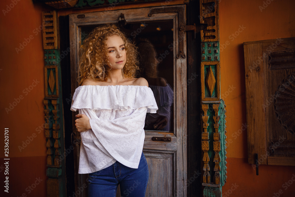 A beautiful young woman with blond curly hair walks through the sunny city