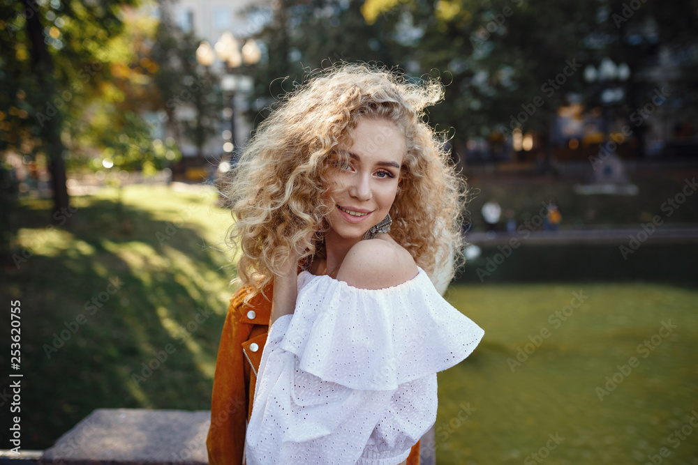 A beautiful young woman with blond curly hair walks through the sunny city A beautiful young woman with blond curly hair walks through the sunny city