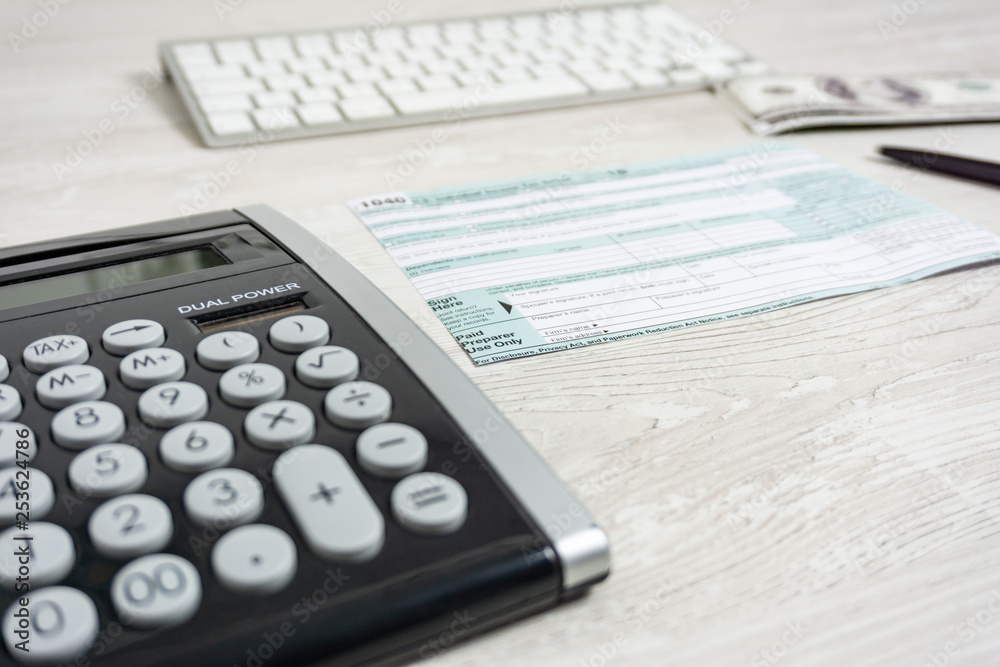 US tax form next to computer keyboard, calculator and tax form 1040. tax form us business income office hand fill concept US tax form next to computer keyboard, calculator and tax form 1040. tax form us business income office hand fill concept