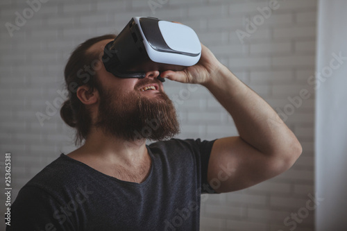 Bearded male hipster looking shocked with his mouth open, wearing virtual reality glasses, copy space. Young man using vr 3d glasses at work. Man trying vr headset. Innovations, technology, digital co