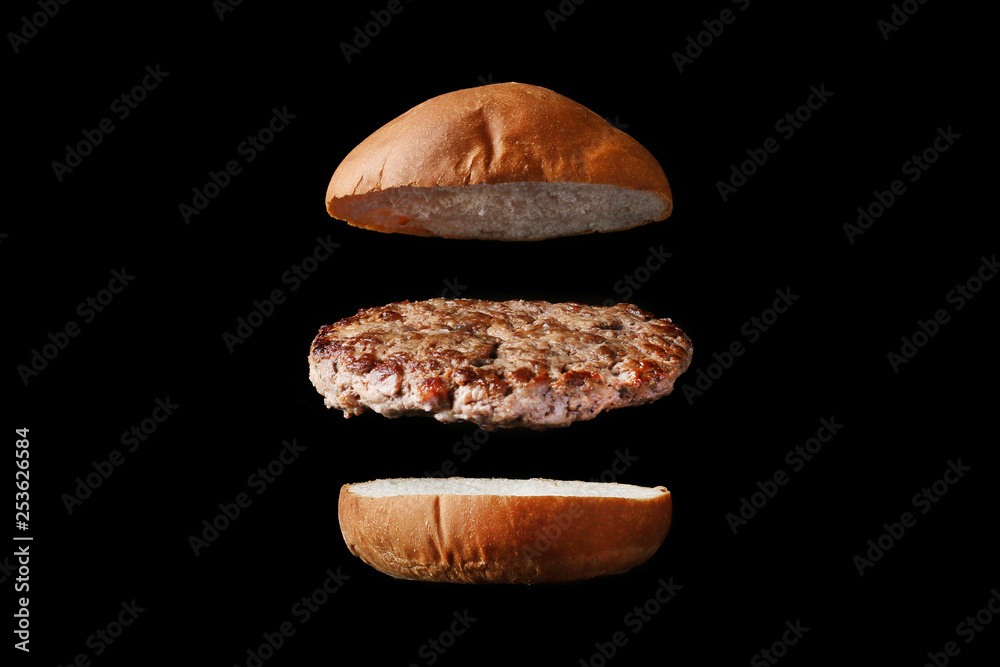 Naklejka premium fly burger isolated on black background. bun and meat