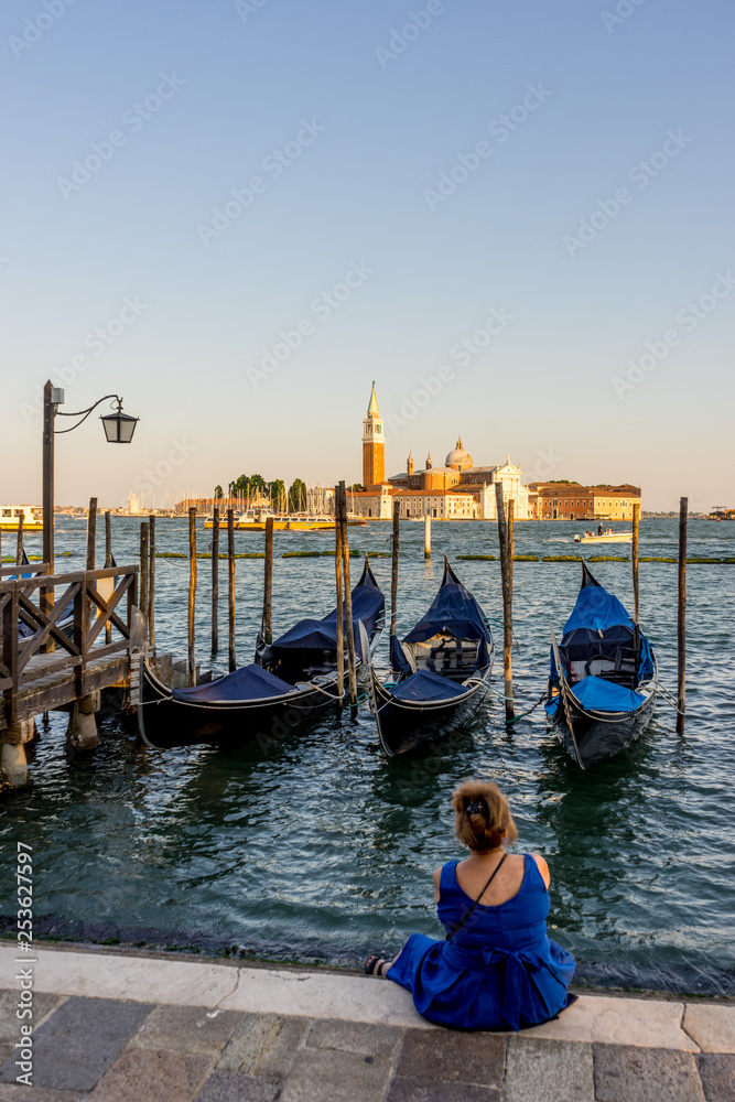 Lady staring at Gondolas moored by Saint Mark square with San Giorgio di Maggiore church in the background in Venice, Italy