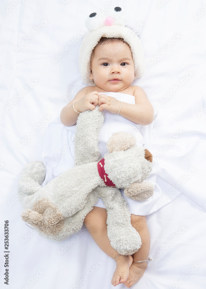 Happy Asian baby girl lying with dog doll on white bed sheets. Happy Asian baby girl lying with dog doll on white bed sheets.