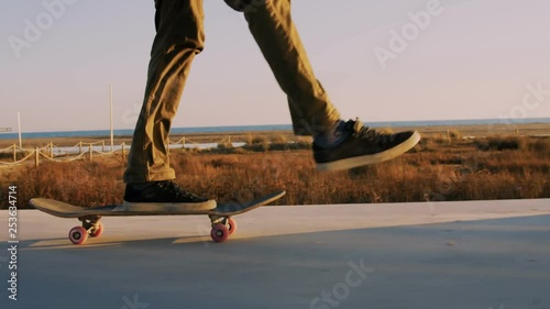 Close up shot of skateboarder legs and feet push skate on empty beach sidewalk. Does trick, pop shuvit by flipping board. Rolls to skatepark or to hangout, teenager afterschool activity fun times photo