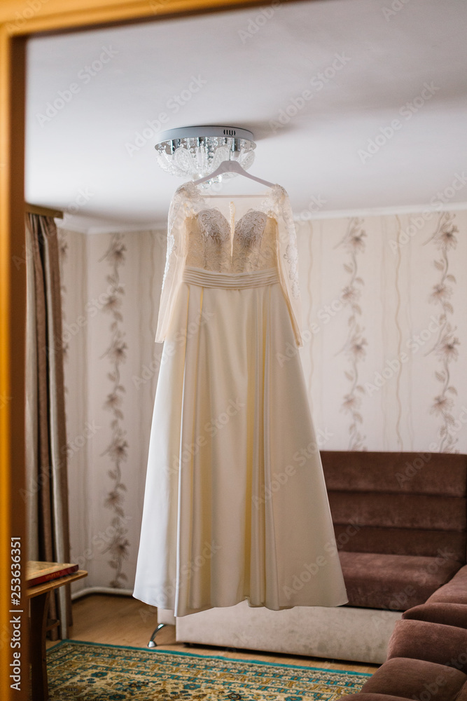 Very beautiful wedding dress of the bride hanging on the chandelier in the room. Very beautiful wedding dress of the bride hanging on the chandelier in the room.