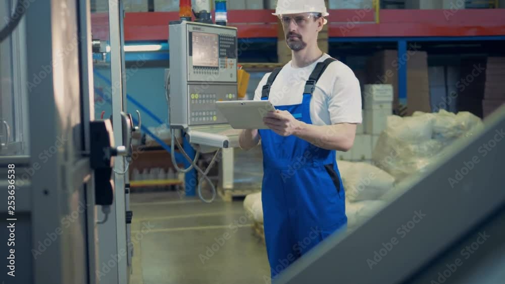 A piece of functioning industrial machine a male worker standing near it A piece of functioning industrial machine a male worker standing near it