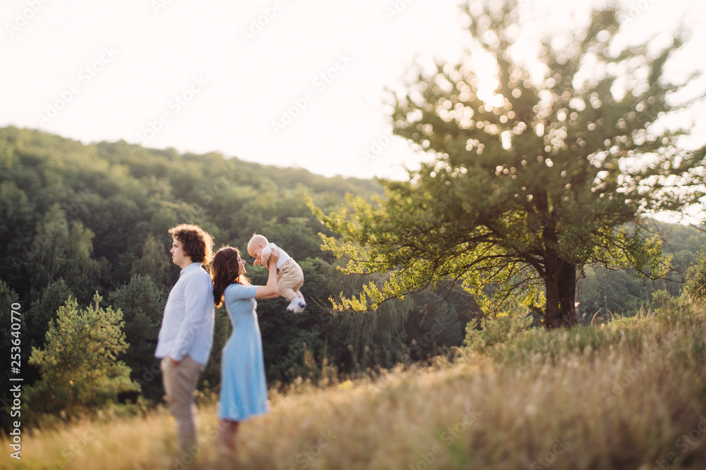 Young happy caucasian couple with little baby boy. Parents and son walking and having fun together. Mother and father playing with toddler outdoors. Family, parenthood, childhood, happiness concept.