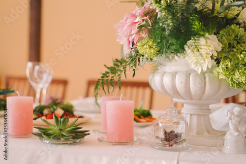 Coziness and style. Modern event design. Table setting at wedding reception. Floral compositions with beautiful flowers and greenery, candles, laying and plates on decorated table.