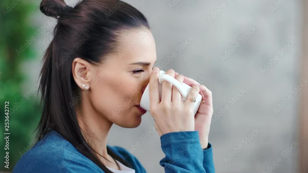 Side view happy charming young woman slowly drinking hot beverage holding big mug Side view happy charming young woman slowly drinking hot beverage holding big mug