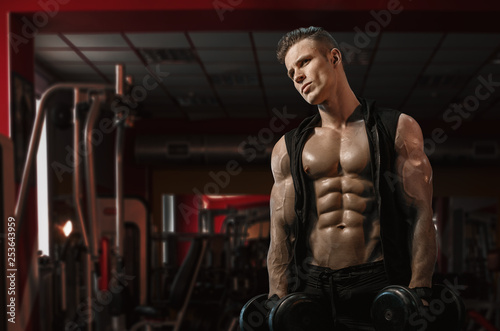 Muscular model sports young man exercising in gym with dumbbell. Portrait of sporty healthy strong muscle. Fitness trainer. Sport workout bodybuilding motivation concept. Sexy torso.