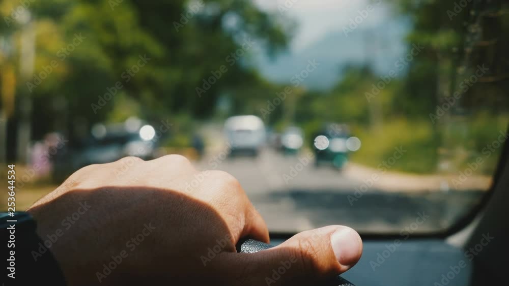 Beautiful in-car close-up, male hand holding steering wheel driving along blurred beautiful sunny road with green trees. Beautiful in-car close-up, male hand holding steering wheel driving along blurred beautiful sunny road with green trees.