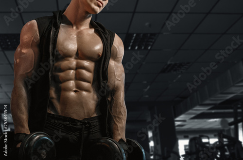 Muscular model sports young man exercising in gym with dumbbell. Portrait of sporty healthy strong muscle. Fitness trainer. Sport workout bodybuilding motivation concept. Sexy torso.