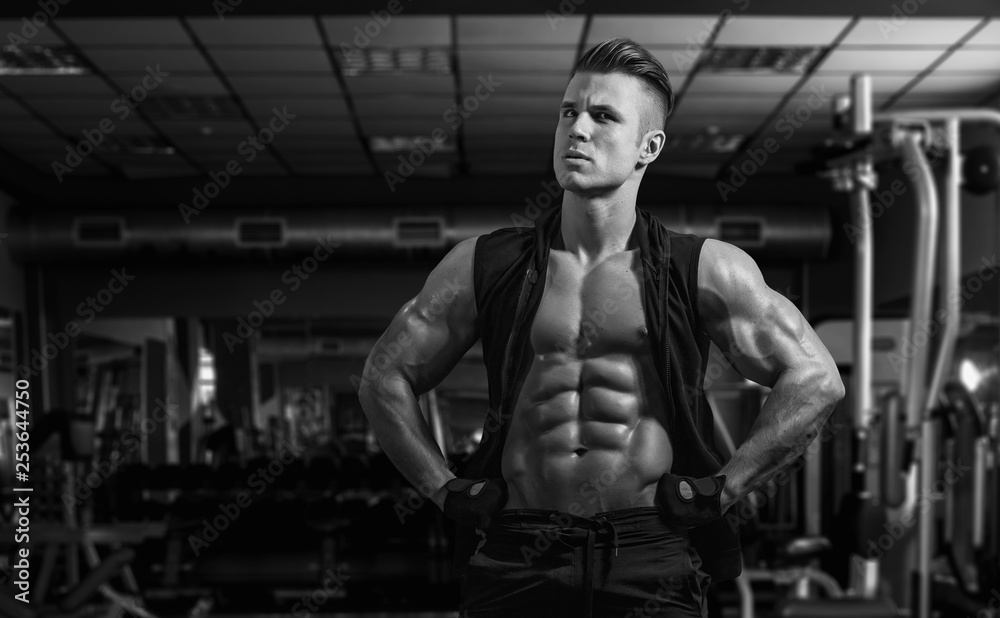 Muscular model sports young man exercising in gym. Black and white portrait of strong muscle. Fitness trainer. Sport workout bodybuilding motivation concept. Sexy torso. Muscular model sports young man exercising in gym. Black and white portrait of strong muscle. Fitness trainer. Sport workout bodybuilding motivation concept. Sexy torso.