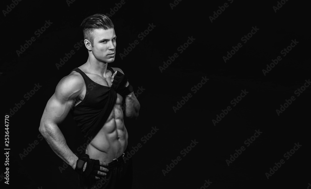 Muscular model young man on dark background. Strong brutal guy showing his biceps triceps, flexing his muscles. Sexy naked torso, six pack abs. Sport workout bodybuilding healthy lifestyle concept.