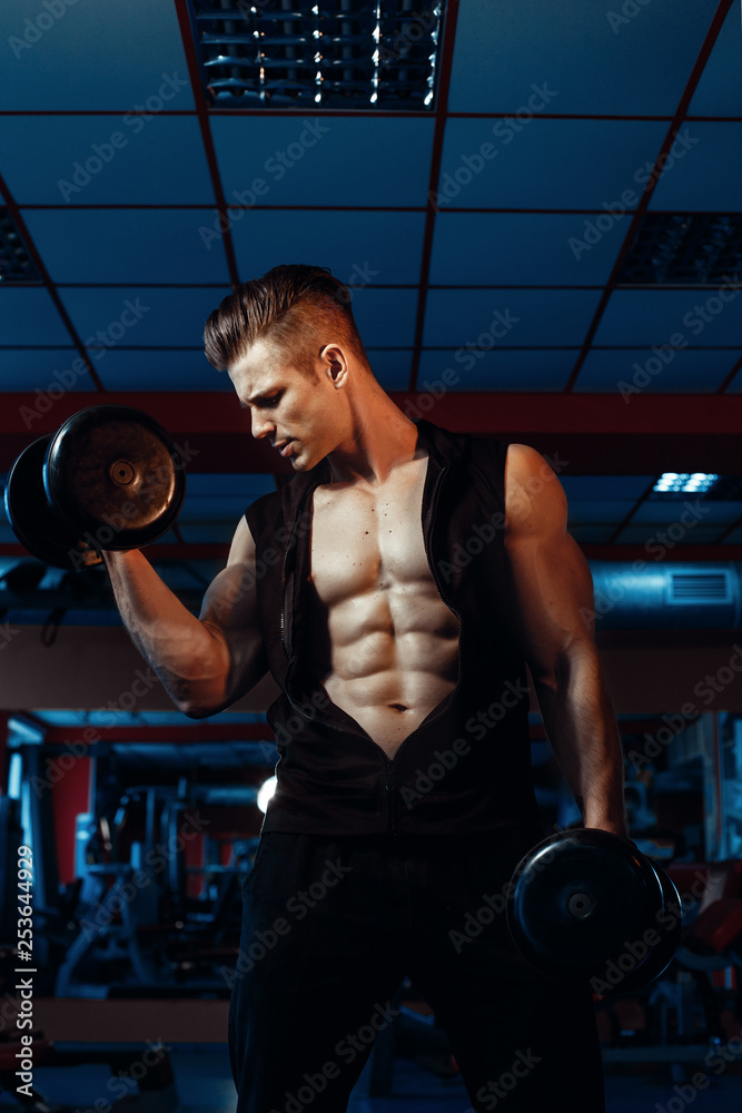 Foto Stock Muscular model sports young man exercising in gym with dumbbell.  Portrait of sporty healthy strong muscle. Fitness trainer. Sport workout  bodybuilding motivation concept. Sexy torso. | Adobe Stock
