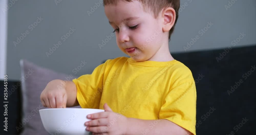 Small Cute Child is Sitting at a Table and eat his own oatmeal, the baby eats willingly. Concept Happy Childhood. Small Cute Child is Sitting at a Table and eat his own oatmeal, the baby eats willingly. Concept Happy Childhood.