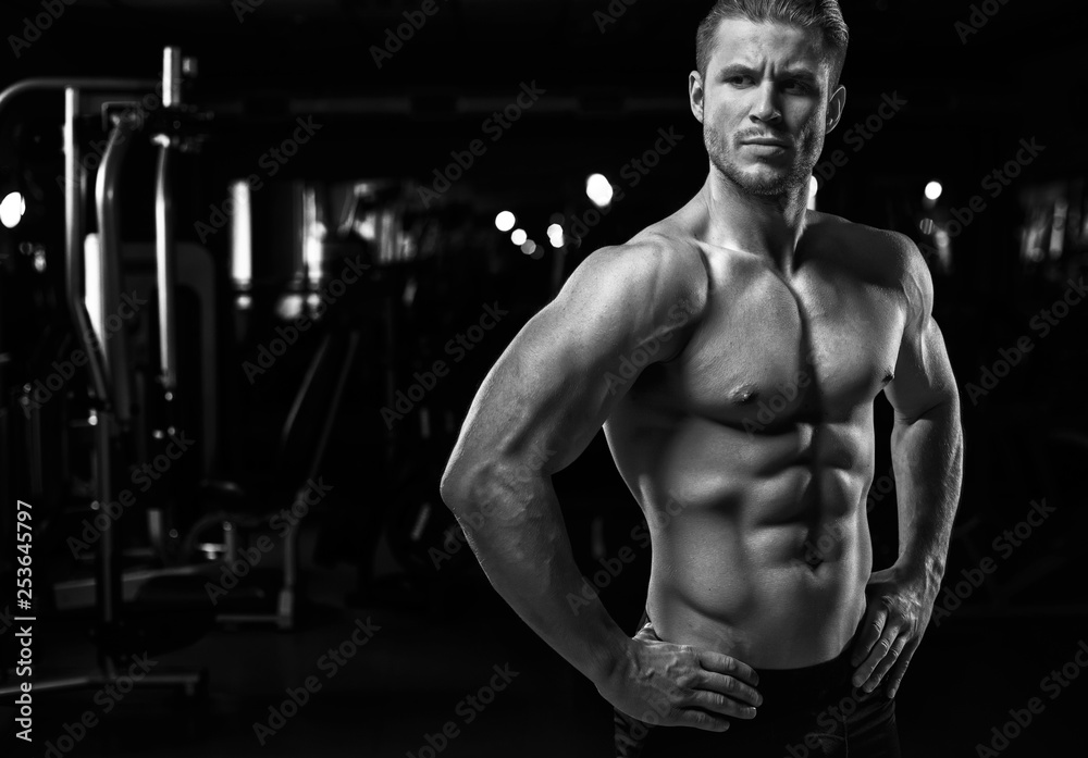 Muscular model sports young man exercising in gym. Black and white portrait of strong muscle. Fitness trainer. Sport workout bodybuilding motivation concept. Sexy torso. Muscular model sports young man exercising in gym. Black and white portrait of strong muscle. Fitness trainer. Sport workout bodybuilding motivation concept. Sexy torso.