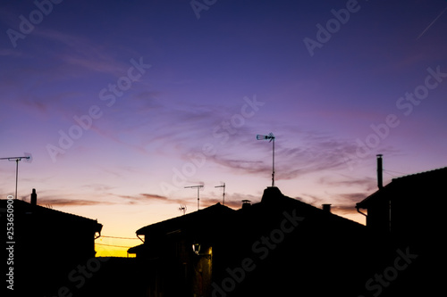 Sunset in the village with silhouettes of antennas and chimneys