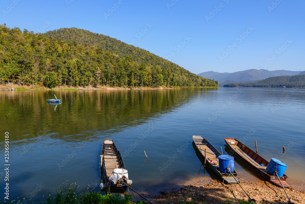 Local wooden long tail boats ground on the shore at Mae NgudSomboonChol dam with background range of mountain , island and lake in Chiang Mai, Thailand.