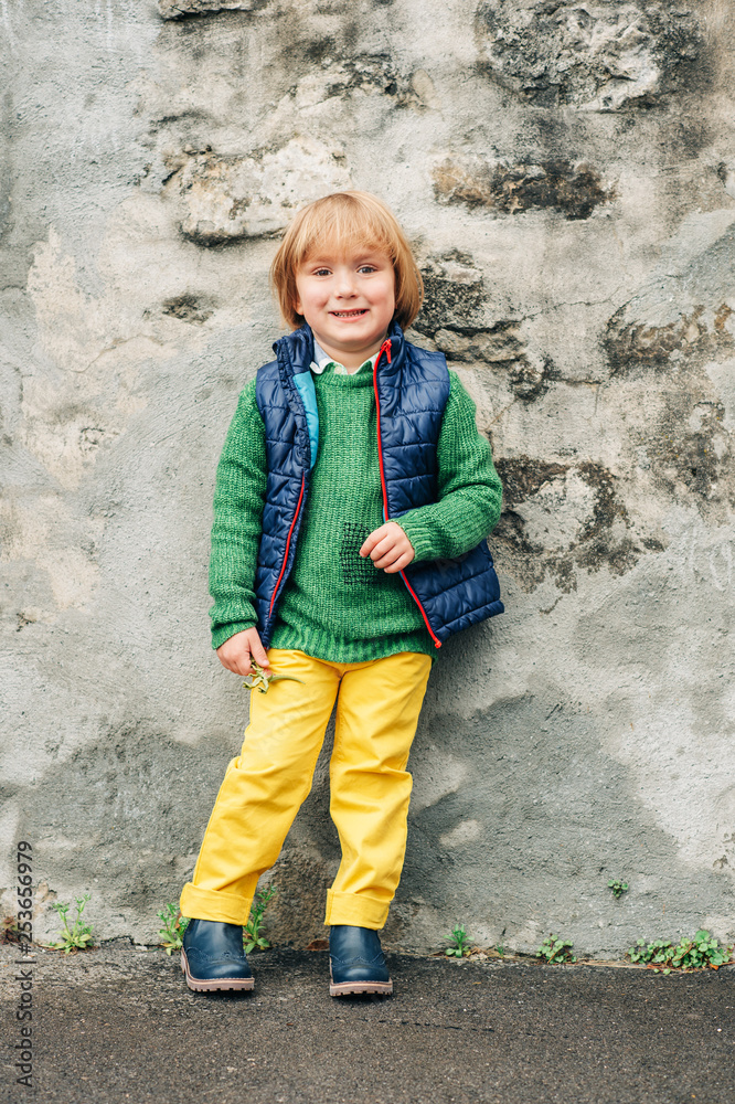 Outdoor fashion portrait of adorable little 4 year old boy, wearing blue waistcoat and boots, yellow trousers and green pullover Outdoor fashion portrait of adorable little 4 year old boy, wearing blue waistcoat and boots, yellow trousers and green pullover