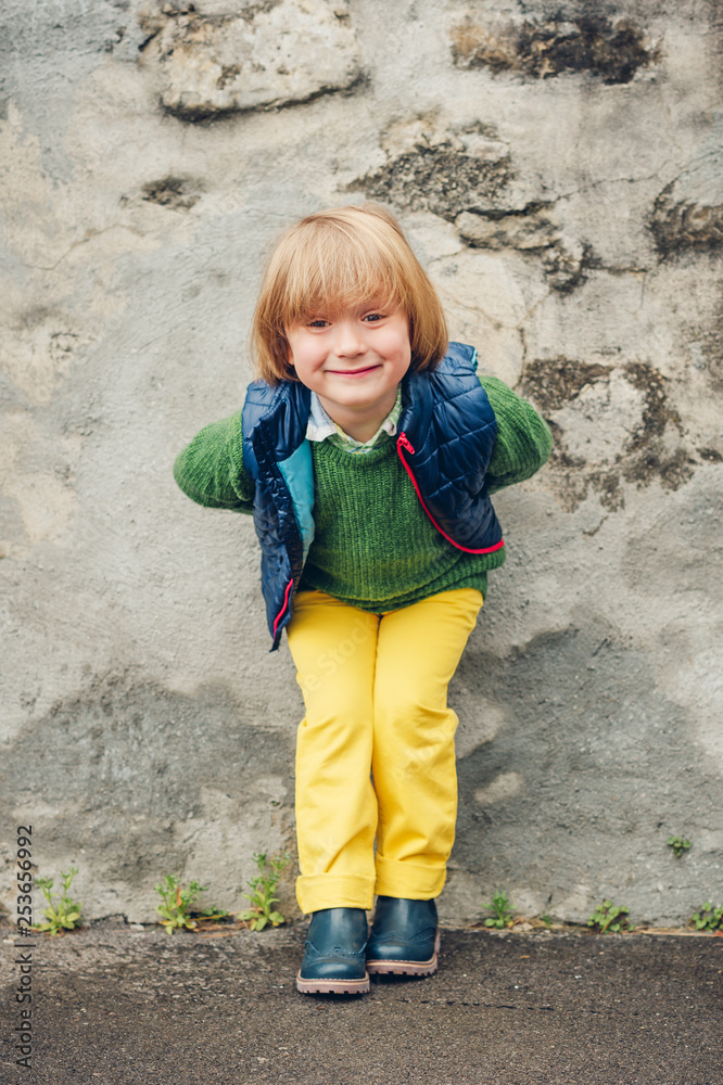 Outdoor fashion portrait of adorable little 4 year old boy, wearing blue waistcoat and boots, yellow trousers and green pullover Outdoor fashion portrait of adorable little 4 year old boy, wearing blue waistcoat and boots, yellow trousers and green pullover