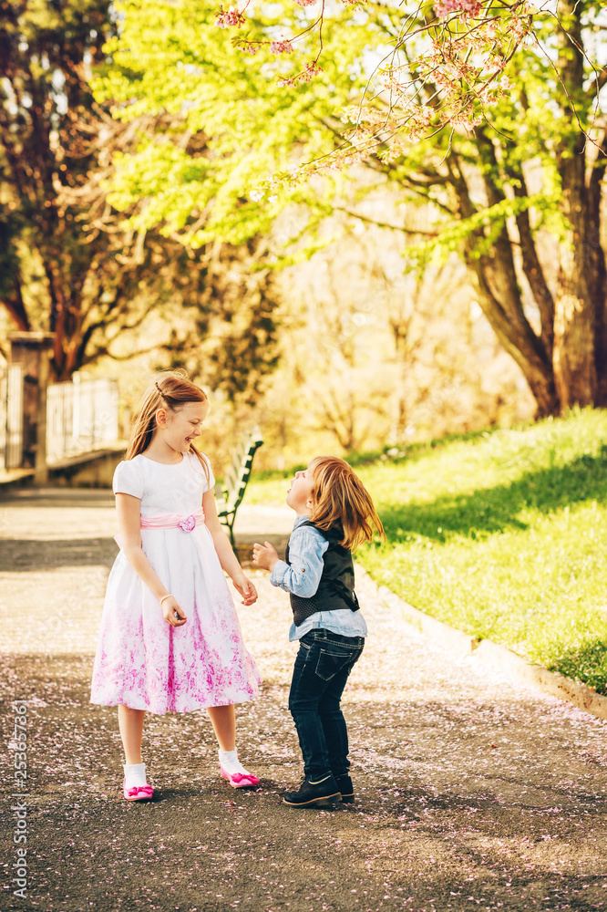 Young girl and boy playing in spring garden, wearing occasion clothes, fashion for young children Young girl and boy playing in spring garden, wearing occasion clothes, fashion for young children