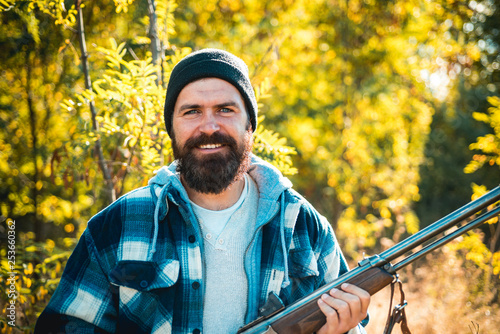 Bearded hunter man holding gun and walking in forest. Hunter with shotgun gun on hunt. Hunting in spring forest. photo