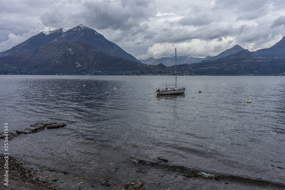 Italy, Varenna, Lake Como, a boat on a body of water with a mountain in the background Italy, Varenna, Lake Como, a boat on a body of water with a mountain in the background