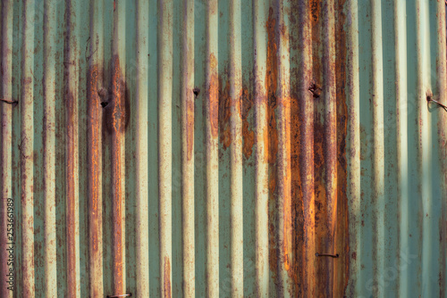 Old green and rusty galvanized, corrugated iron siding vintage texture background of grunge. Image taken with beautiful sun light cast on.